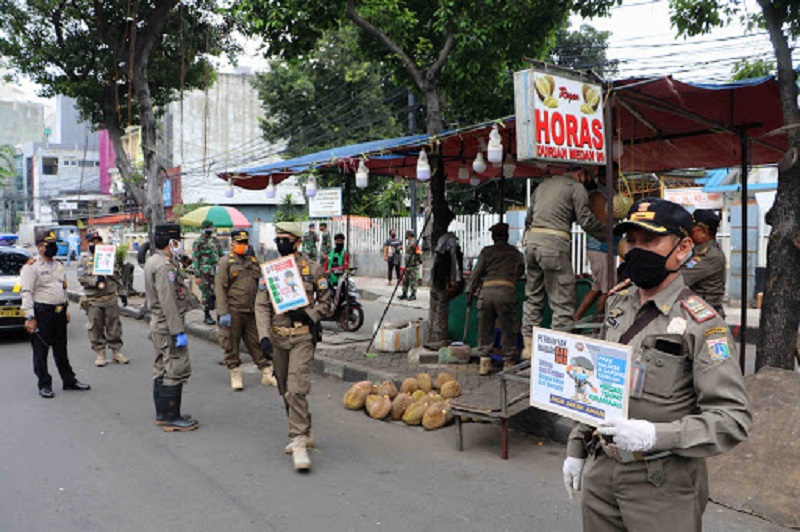 Petugas membantu menutup toko durian yang masih berjualan pada hari pertama penerapan aturan Pembatasan Sosial Berskala Besar (PSBB) di Glodok, Jakarta, Jumat (10/4/2020).  (infopublik.id)